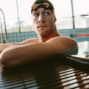 Shot of professional male swimmer resting on the edge of swimming pool. Young man on the edge of pool.