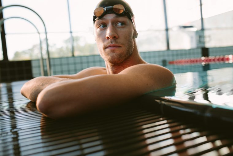 Shot of professional male swimmer resting on the edge of swimming pool. Young man on the edge of pool.