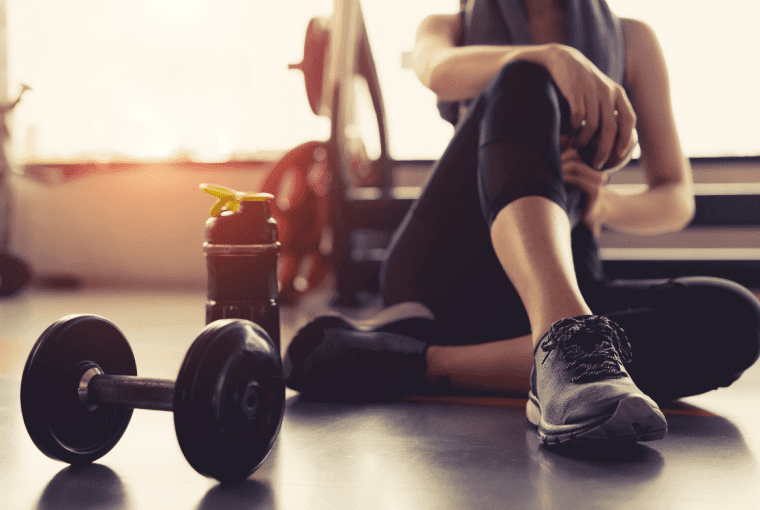 a woman seated on the floor in the gym surrounded by gym equipment