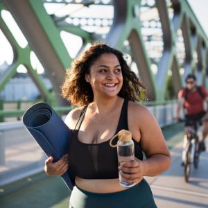 a woman carrying her yoga mat across a bridge