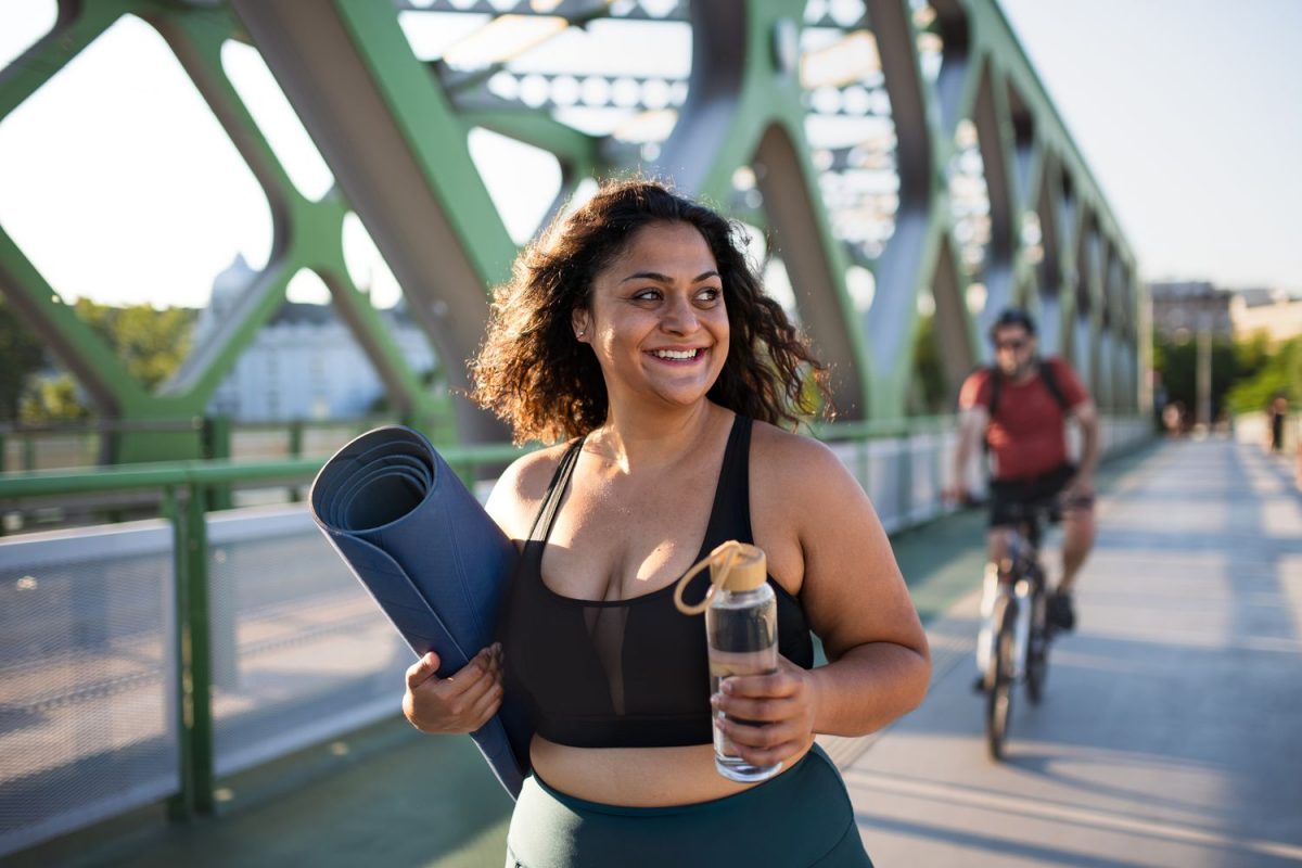 a woman carrying her yoga mat across a bridge