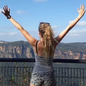 Woman standing with arms raised in front of canyon.