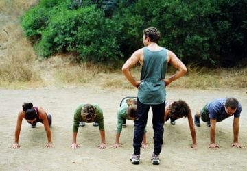 Man standing over group of people doing pushups, rear view