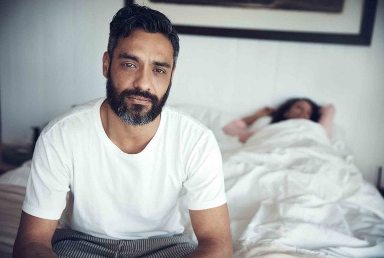 Portrait of a mature man looking upset while his wife sleeps in the background