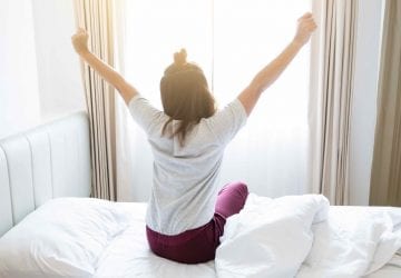 woman raising arms in front of her window after a good night sleep