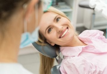Horizontal color close-up headshot of woman having dental examination and sincerely smiling at dentist.