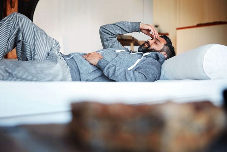 man laying on couch holding his forehead
