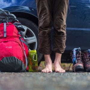 person with bare feet standing next to their hiking gear