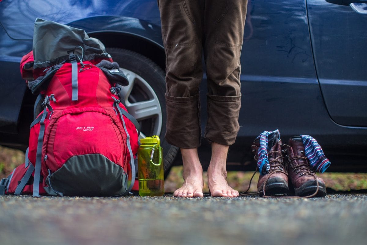 person with bare feet standing next to their hiking gear