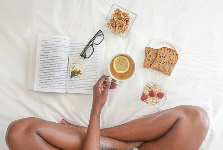 woman sitting on bed having breakfast and reading a book
