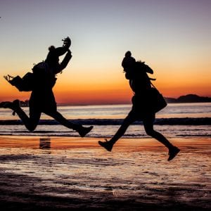 two people jumping in the air at the beach
