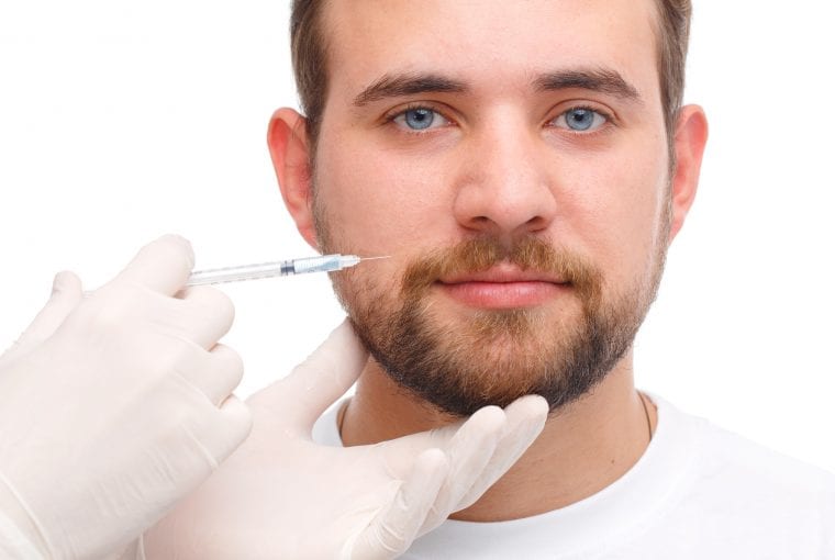 A male doctor is injected by a doctor wearing white gloves, botox on the cheek near the mouth. Photo on white background