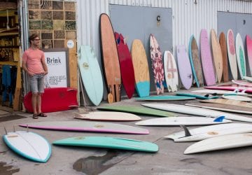 man standing beside a number of different surfboards