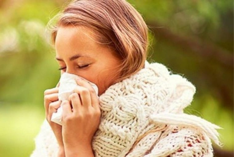 a woman outdoors sneezing into a kleenex