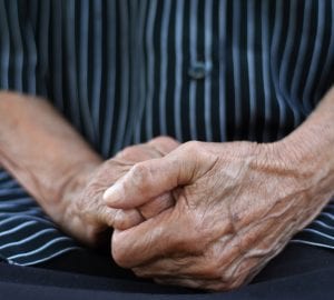 Close up of a midsection of an old woman, hand in hand in lap, wearing black short with white straps