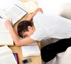 a boy asleep on his desk with books and paper scattered around him