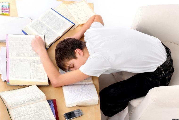 a boy asleep on his desk with books and paper scattered around him