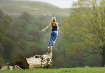 woman standing on the edge of a log lifting up to the sty