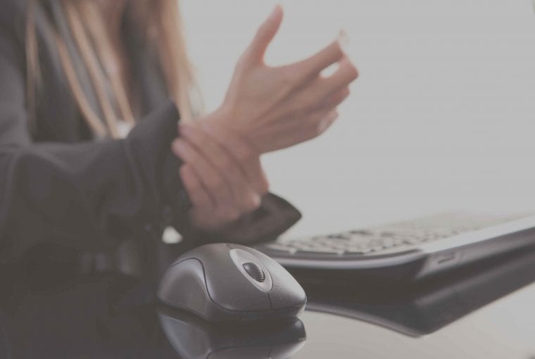 woman rubbing her wrists next to her computer keyboard and mouse