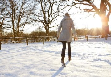 Young woman walking in the snow into the sunset