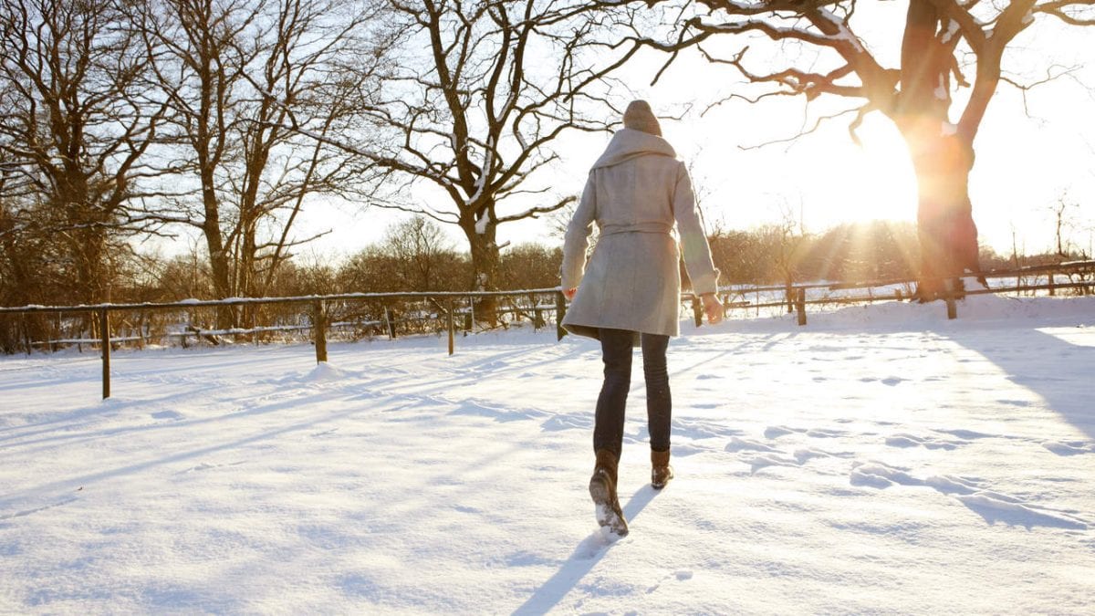 Young woman walking in the snow into the sunset
