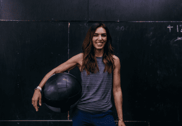 a fit woman standing in the gym with a medicine ball