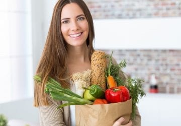 woman standing in her kitchen with a bag of groceries