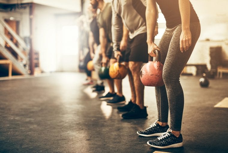 Fit group people in exercise gear standing in a row holding dumbbells during an exercise class at the gym