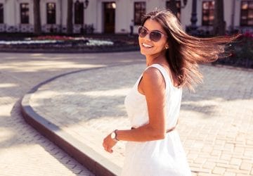 Happy woman in sunglasses and dress walking outdoors. Looking at camera