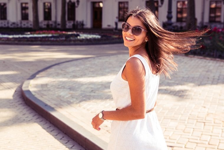 Happy woman in sunglasses and dress walking outdoors. Looking at camera