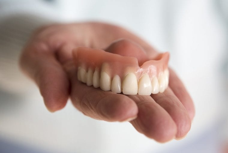 closeup of older womans hand holding a teeth denture