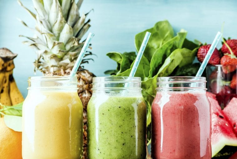 Freshly blended fruit smoothies of various colors and tastes in glass jars. Yellow, red, green. Turquoise blue background