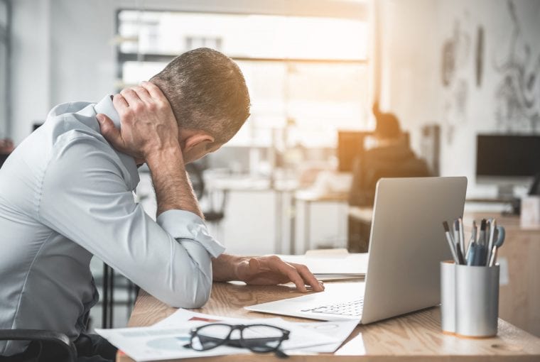 Man holding sore neck while using notebook computer. He sitting at table. Sick worker concept