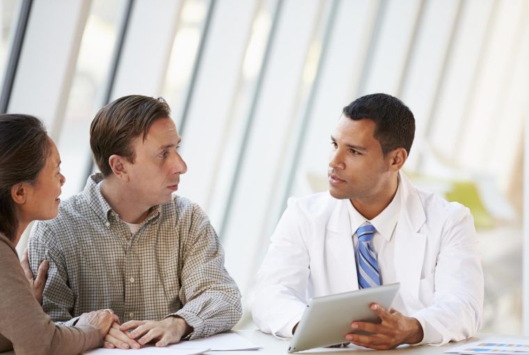 Doctor Using Tablet Computer Discussing Treatment With Patients In Meeting