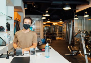 A portrait of a gym owner while wearing a protective face mask at the entrance of the gym.