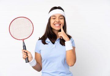 a girl holding a racquet and pointing to her teeth