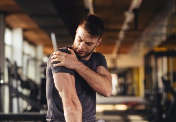 young man feeling the pain in shoulder at the gym