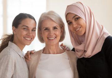 Three happy beautiful diverse two generation women young asian muslim woman wear hijab and caucasian older mature female multicultural ladies bonding standing together looking at camera, portrait