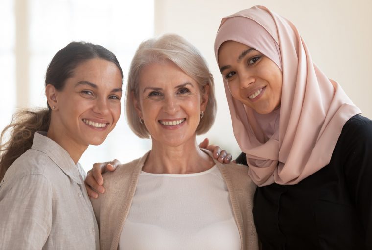Three happy beautiful diverse two generation women young asian muslim woman wear hijab and caucasian older mature female multicultural ladies bonding standing together looking at camera, portrait
