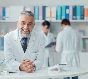 Smiling confident doctor at the reception desk, medical staff working on the background