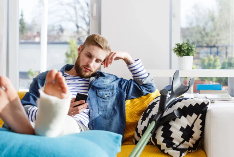 a man sitting on his couch with a leg cast scrolling on his phone