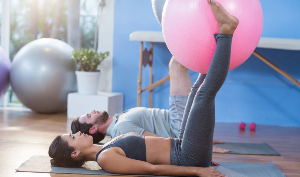 Man and woman holding exercise ball between legs in the clinic