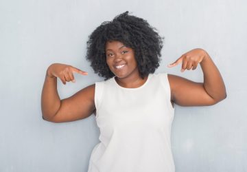 Young african american woman over grey grunge wall looking confident with smile on face, pointing oneself with fingers proud and happy.