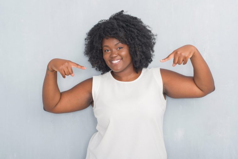 Young african american woman over grey grunge wall looking confident with smile on face, pointing oneself with fingers proud and happy.