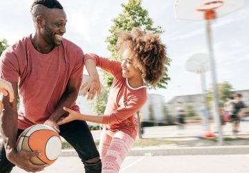 a dad and his daughter outdoors playing basketball