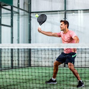 Man playing padel in a green grass padel court indoor behind the net