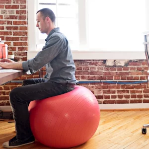 a man sitting on a mobility ball at a desk