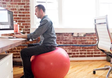 a man sitting on a mobility ball at a desk