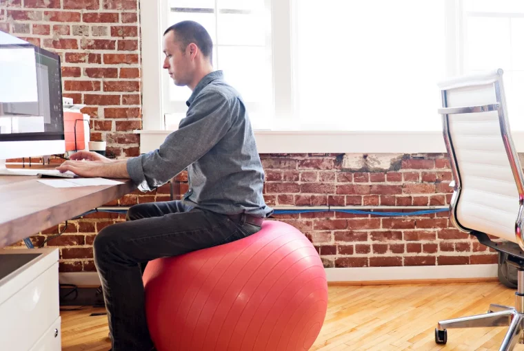 a man sitting on a mobility ball at a desk