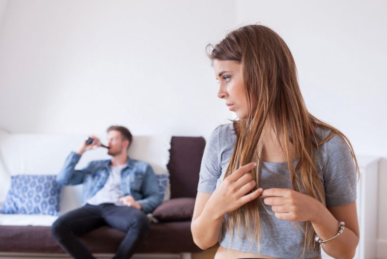 a woman looking back at a man drinking a beer